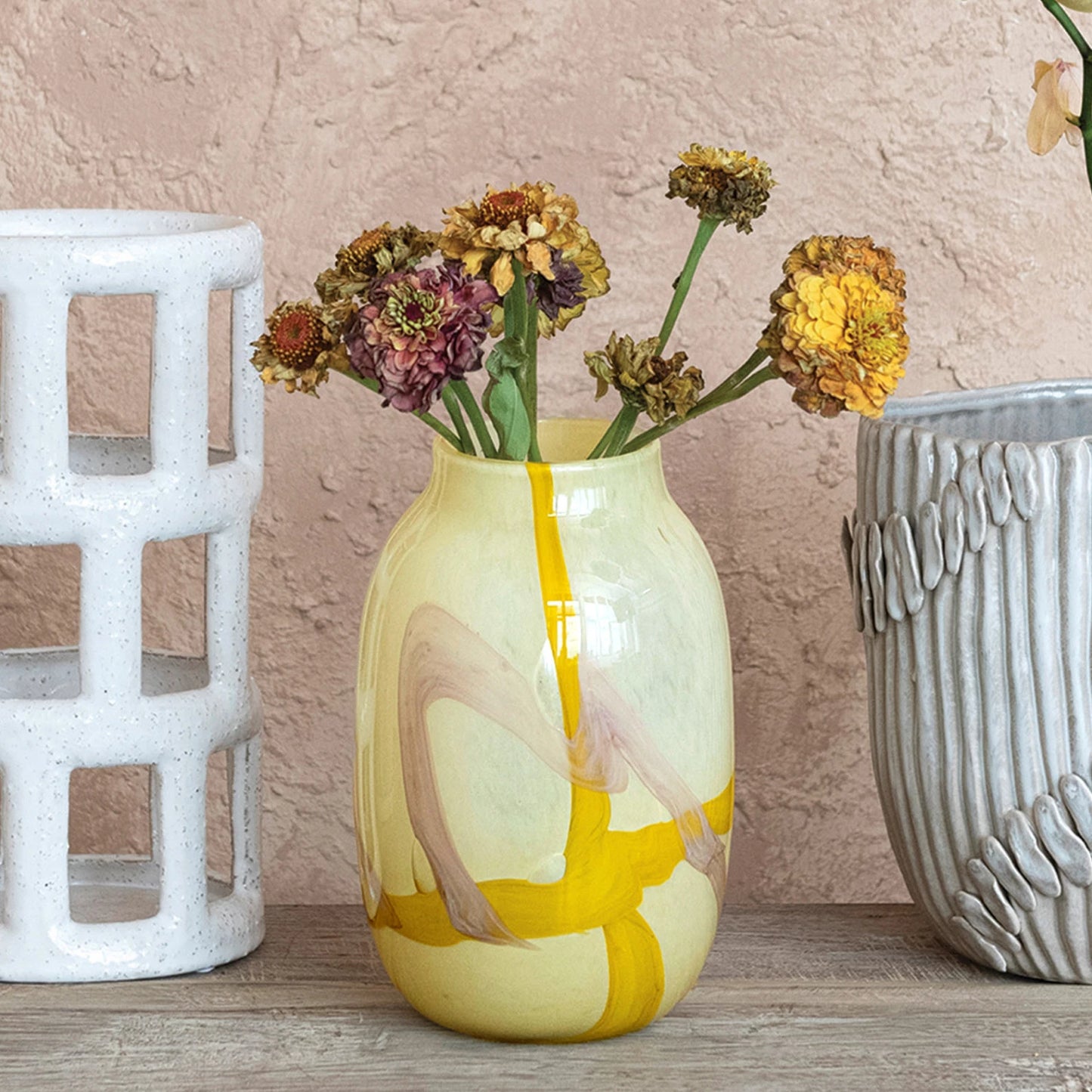 Yellow vase with artistic design and dried flowers on a wooden surface
