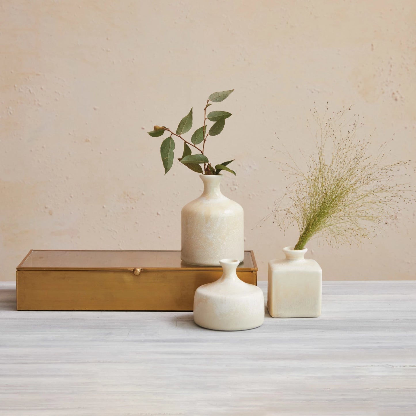 3 sizes and shapes of vases arranged on a table with a wooden box, sprigs of greenery are in 2 of the vases.