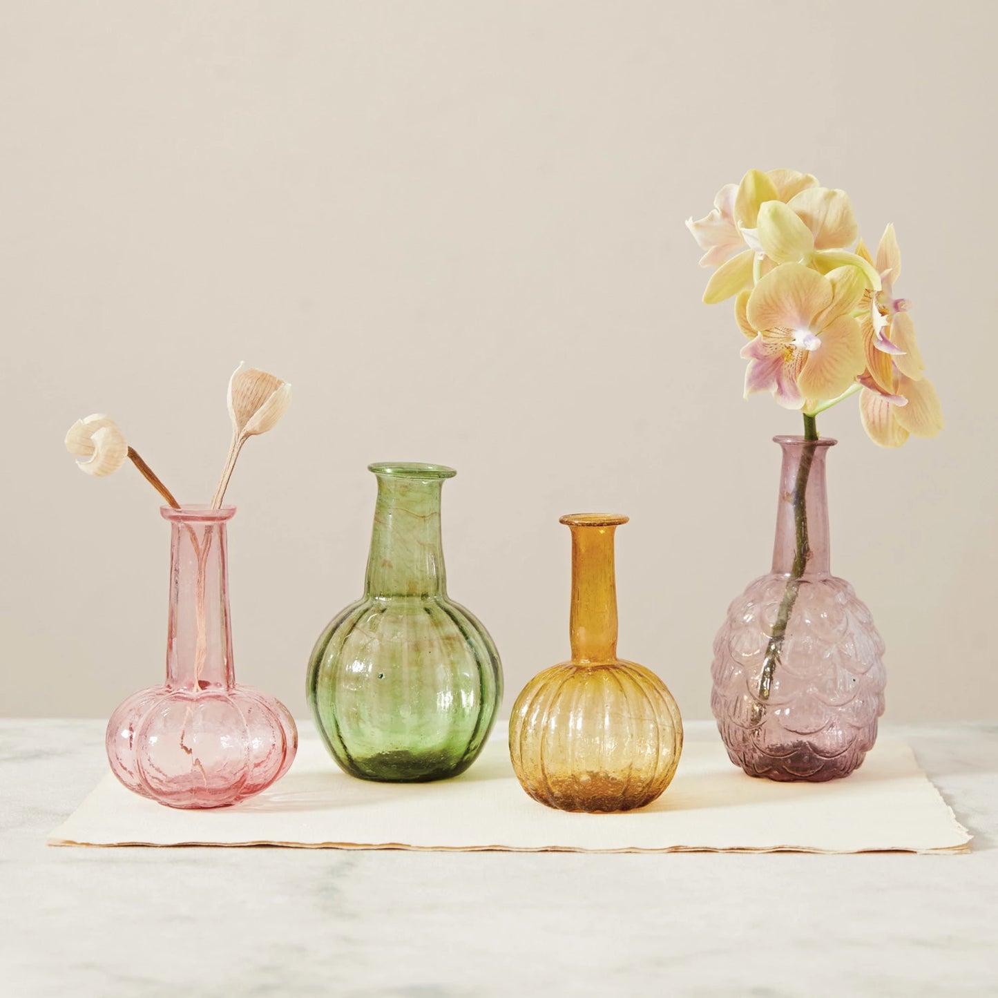 3 colors and designs of recycled glass vases on  table, 2 of them have floral in them.