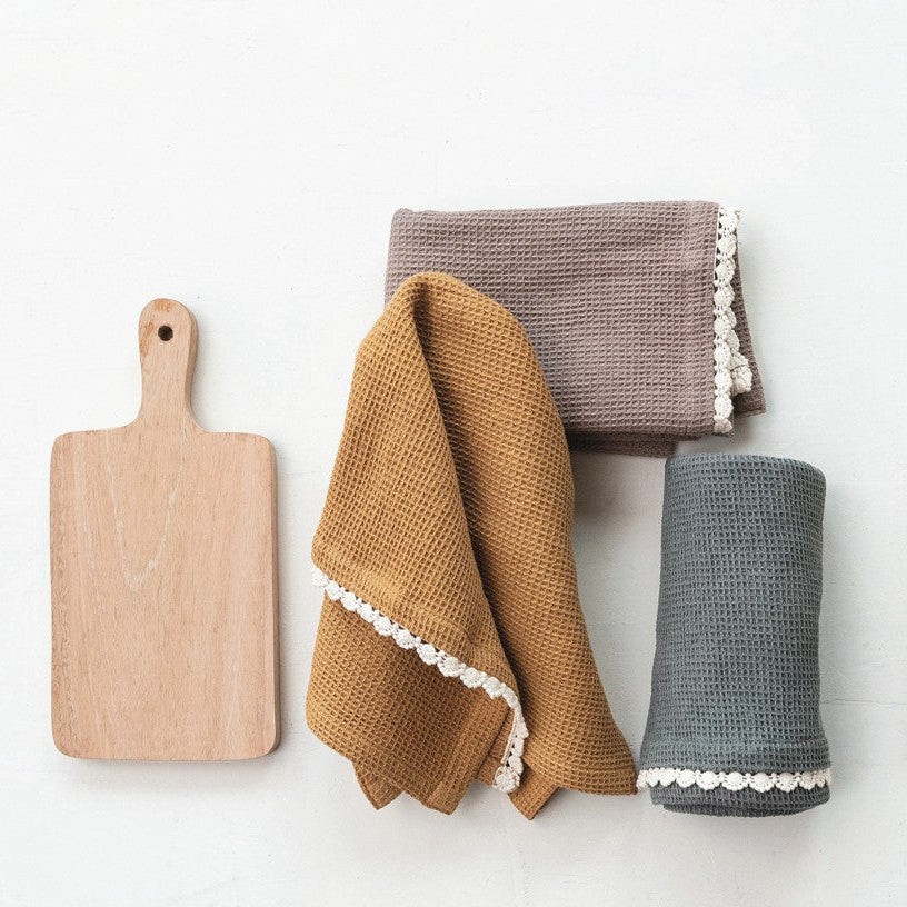 wood board and 3 different colored tea towels folded up