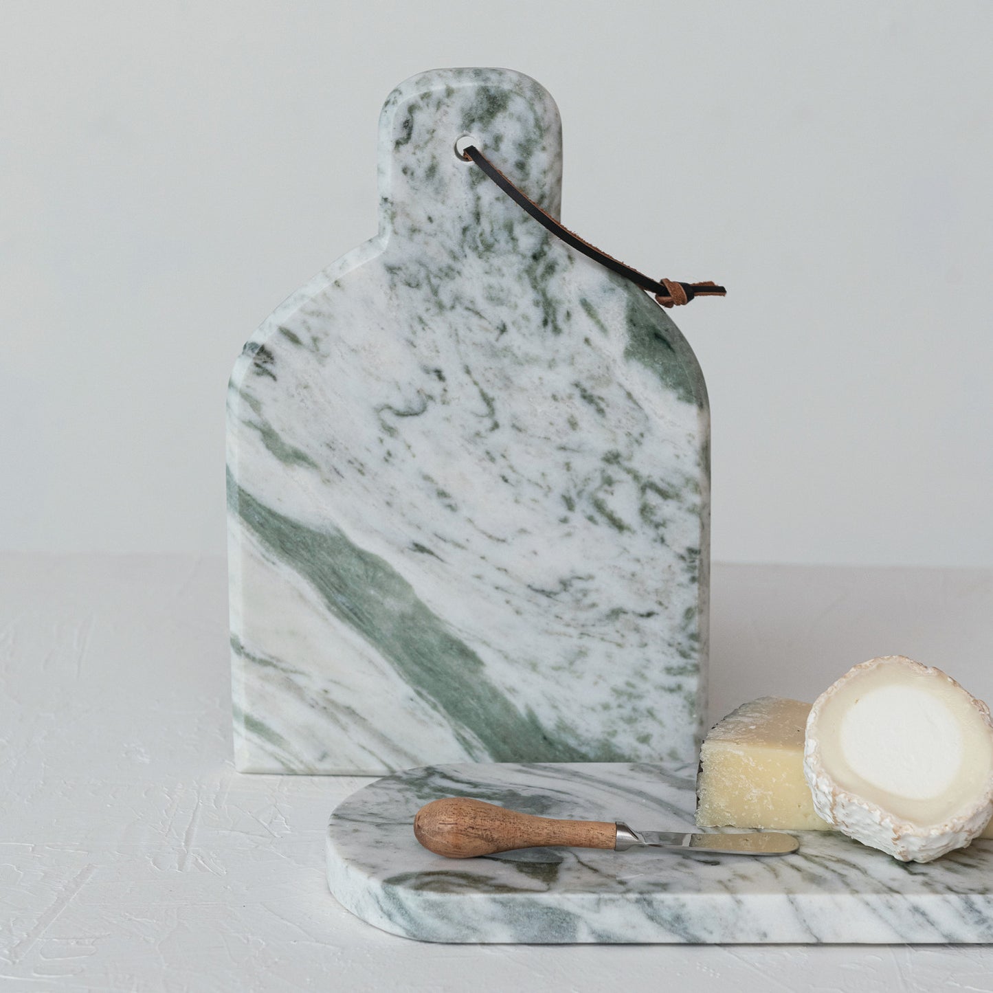 Marble cutting board with knife and cheese on a light gray background