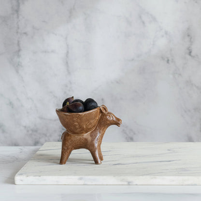 brown ceramic donkey with a small bowl on its back filled with figs set on a marble surface.
