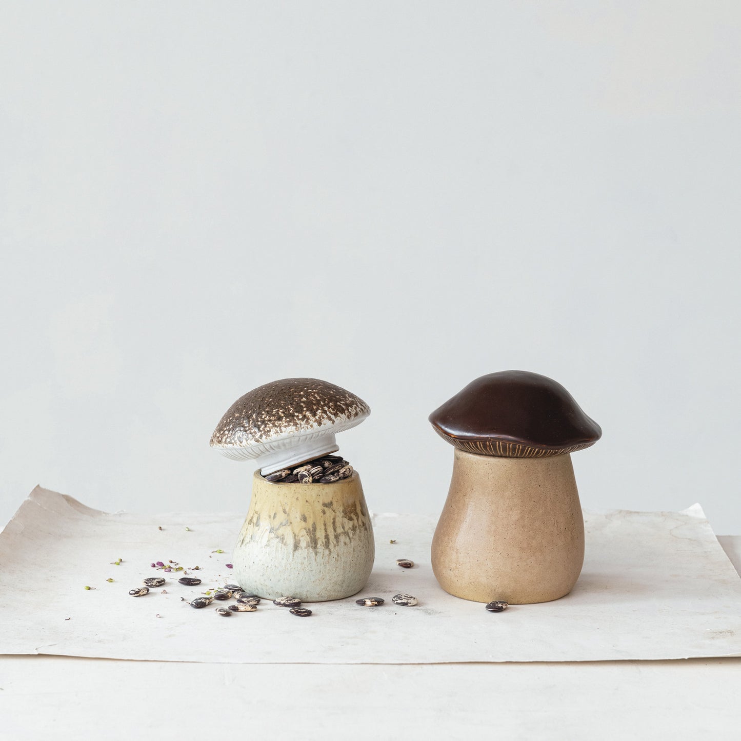 2 styles of mushroom canisters set on a table with sunflower seed in one of them.