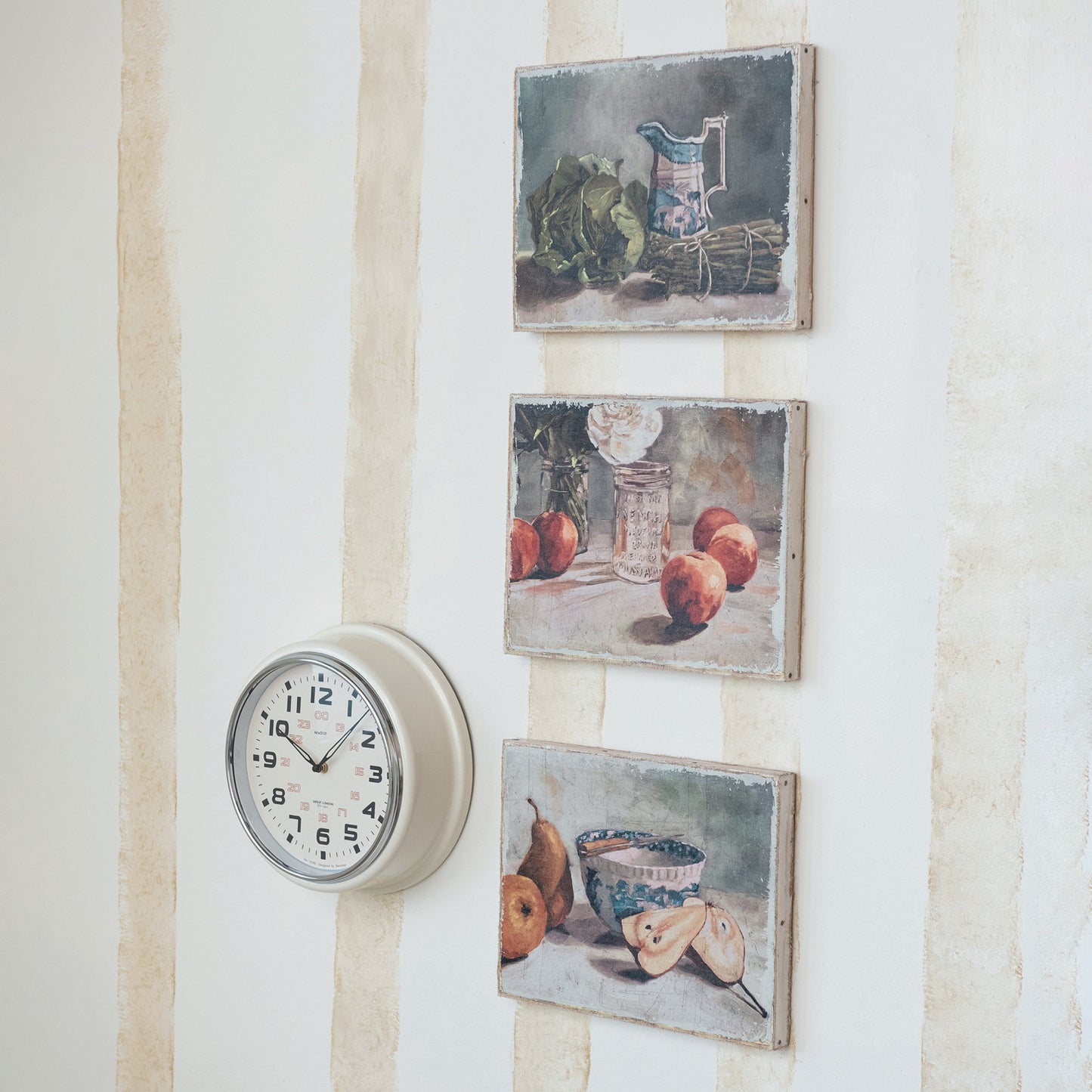 three framed still life paintings displayed on a wall alongside a round white clock.