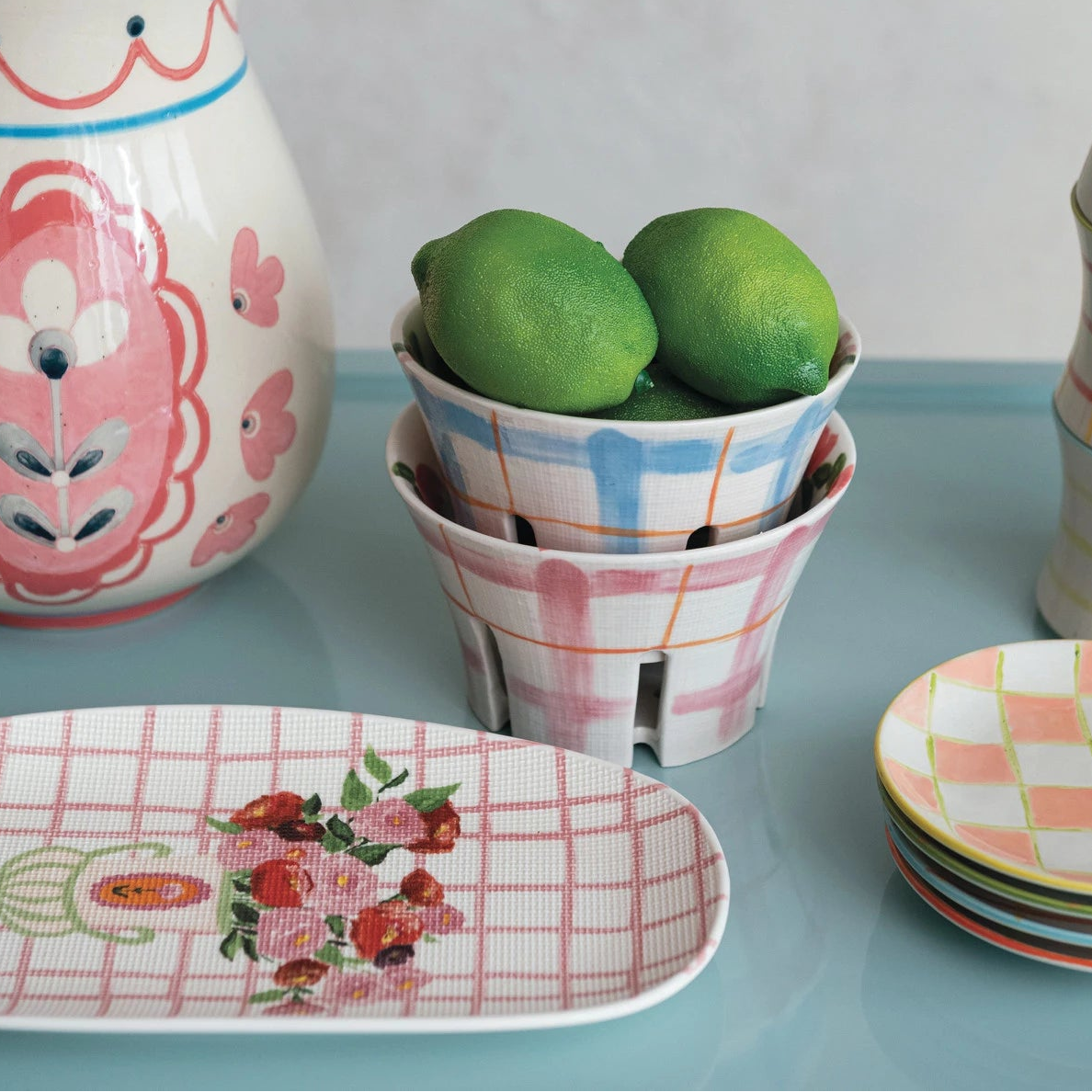 Decorative ceramic items including a pitcher, berry bowls, and plates on a light blue surface.