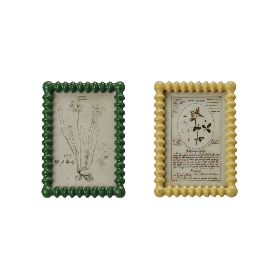 Two vintage inspired picture frames with botanical prints, one with a green border and the other with a yellow border, both with glass covers.