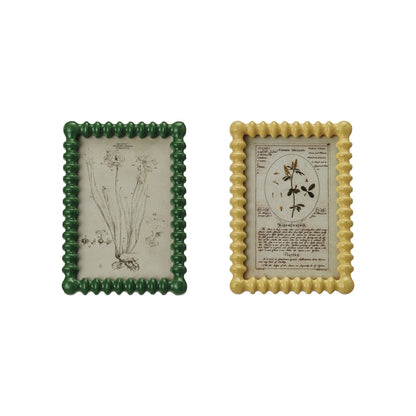 Two vintage inspired picture frames with botanical prints, one with a green border and the other with a yellow border, both with glass covers.
