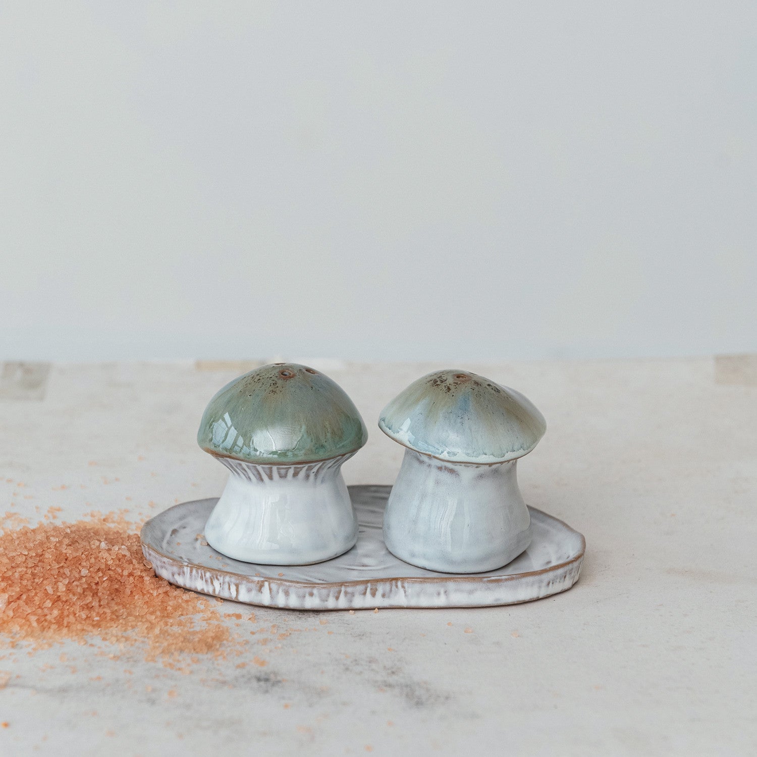 mushroom shaped shakers set on a tray on a countertop with a pile of coarse salt next to it.