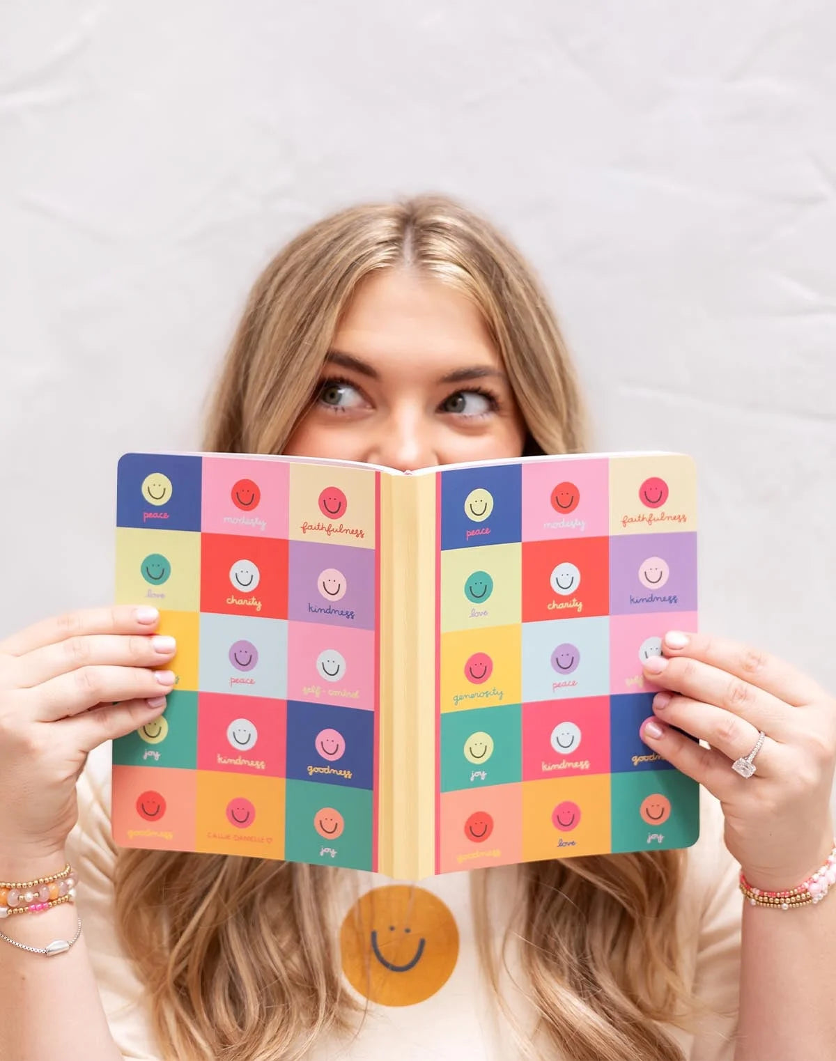 person holding a colorful checkered notebook with smiley face design