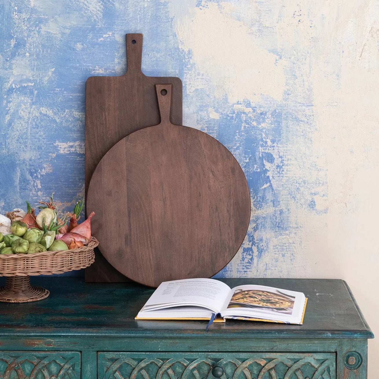 Two wooden cutting boards on a rustic green cabinet with a blue and white distressed wall background.