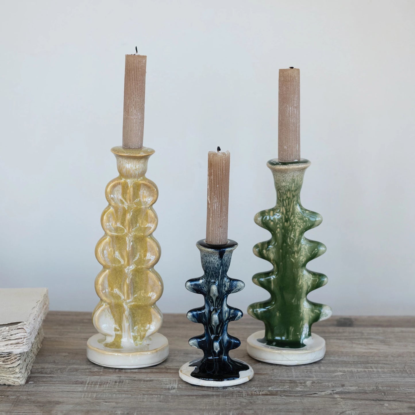 Three ceramic candle holders with candles on a wooden surface.