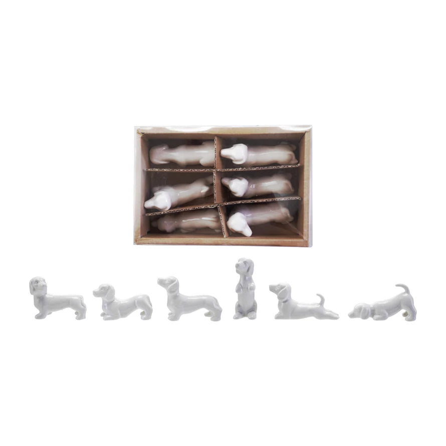 Set of white ceramic dog figurines and  a box containing similar figurines on a white background.