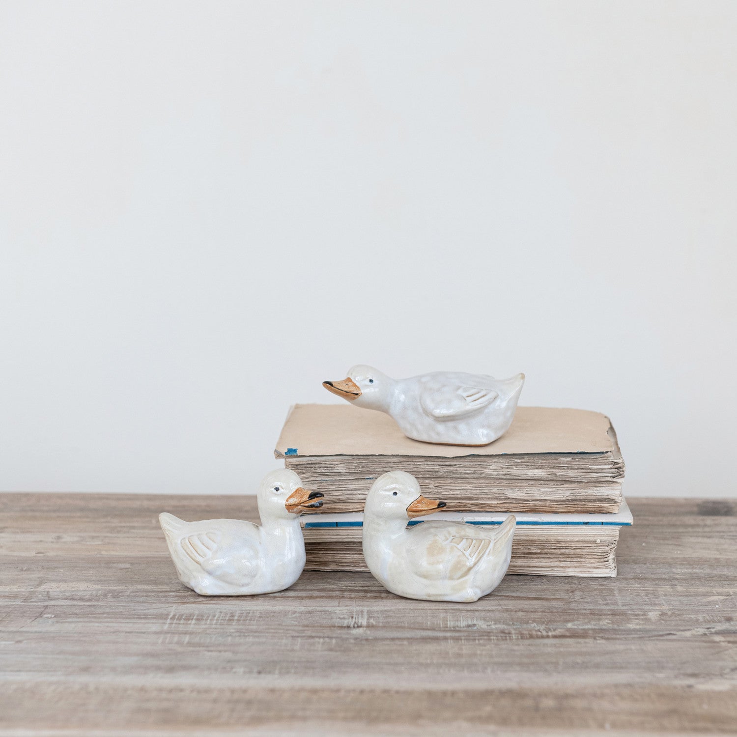 3 stoneware vintage style ducklings sitting on a decorated table and books