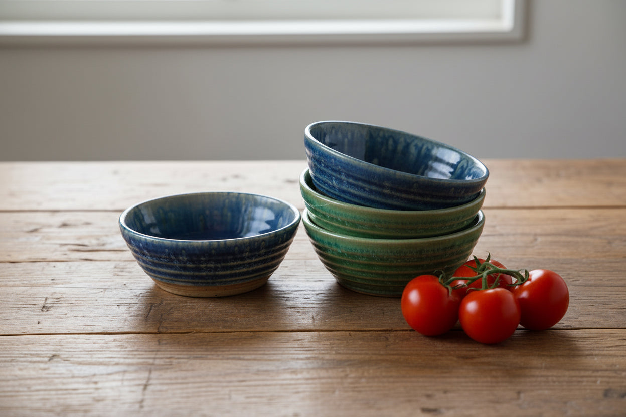 Stacked blue and green ceramic bowls on a wooden surface with tomatoes.