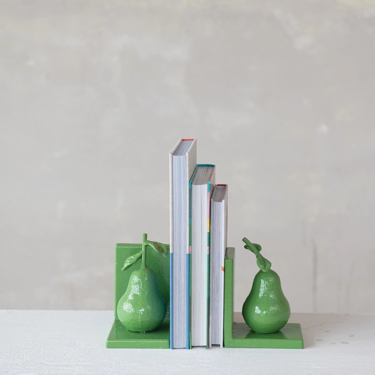 Green pear-shaped bookends holding 3 books on a white surface with a light gray background