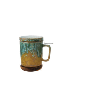 ceramic lidded  green and mustard mug with handle and metal tea strainer, on a plain white background.