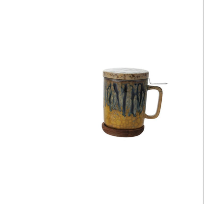 ceramic lidded  blue and mustard mug with handle and metal tea strainer, on a plain white background.