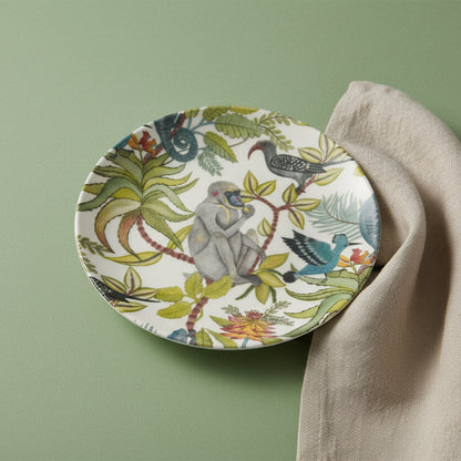 salad plate with monkey, bird, and greenery pattern shown on a pale green background with a linen napkin