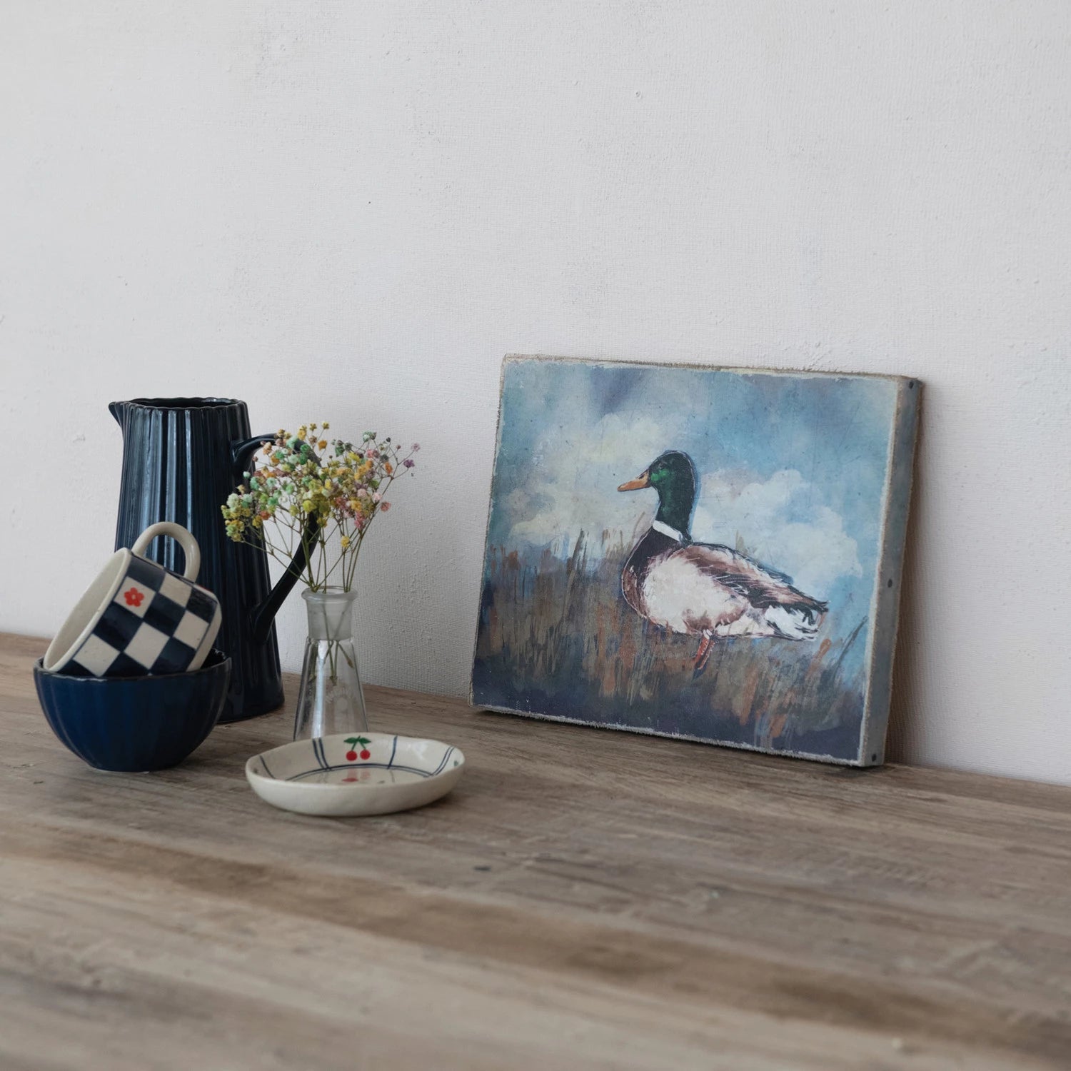 Decorative items including a pitcher, cups, vase with flowers, and a painting of a duck on a wooden surface.