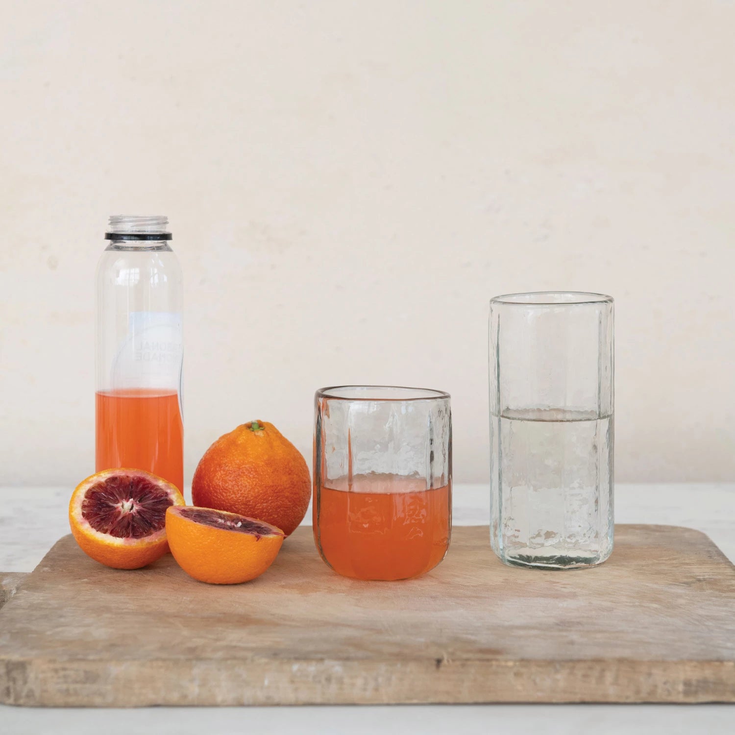 Clear glass bottle and glasses with orange juice on a wooden board