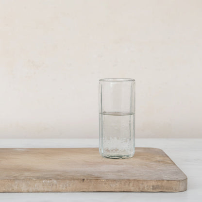 Clear glass half filled with water on a wooden cutting board with a plain background