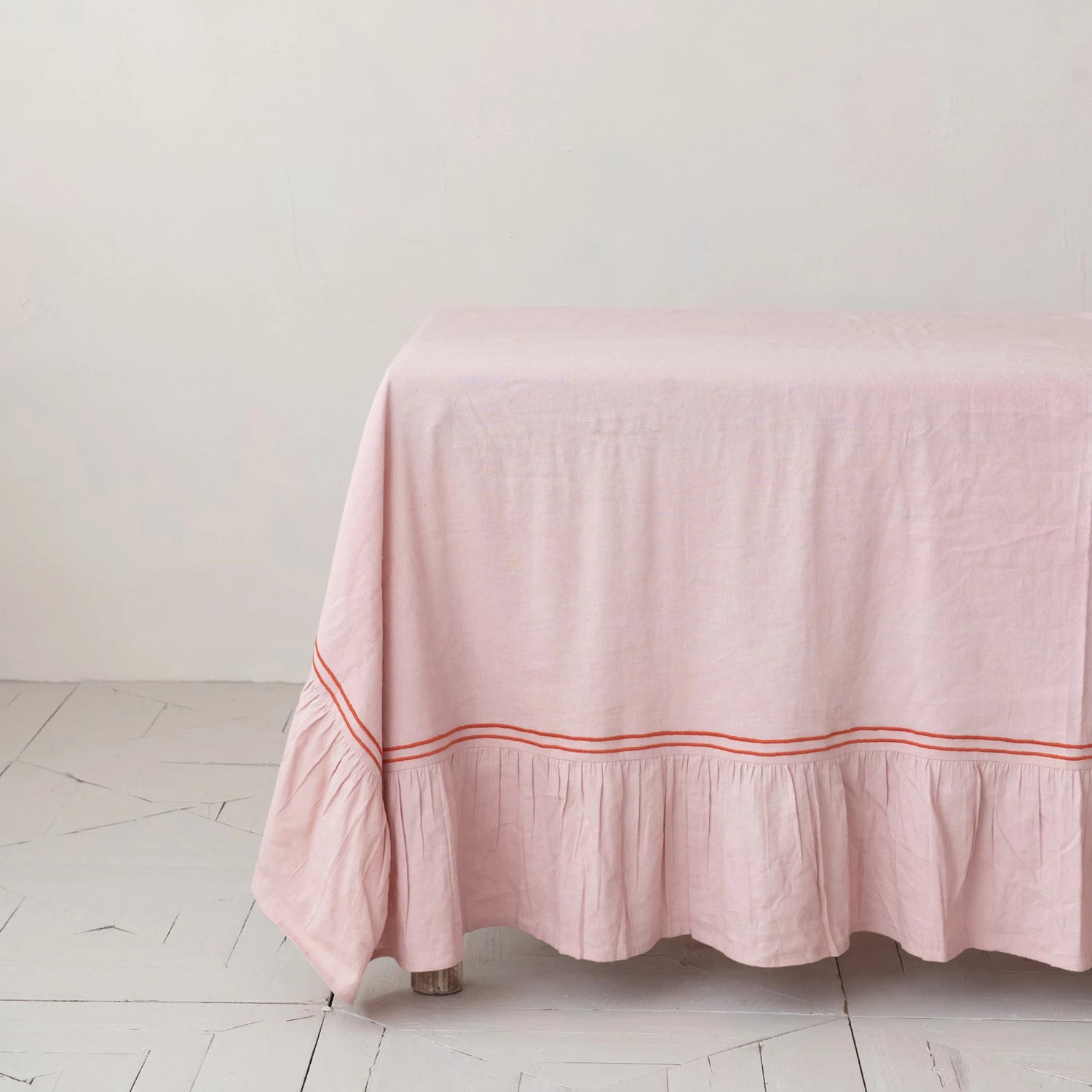 Pink tablecloth with a red stripe laying a table on a white wooden floor and light gray wall.