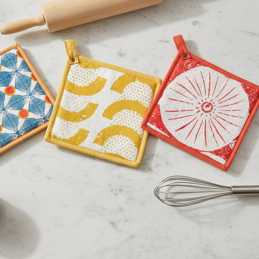 Three colorful pot holders on a marble surface with kitchen tools.
