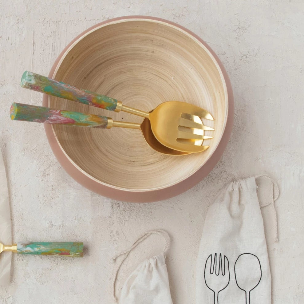 Set of gold serving utensils with colorful handles in a serving bowl on a neutral background