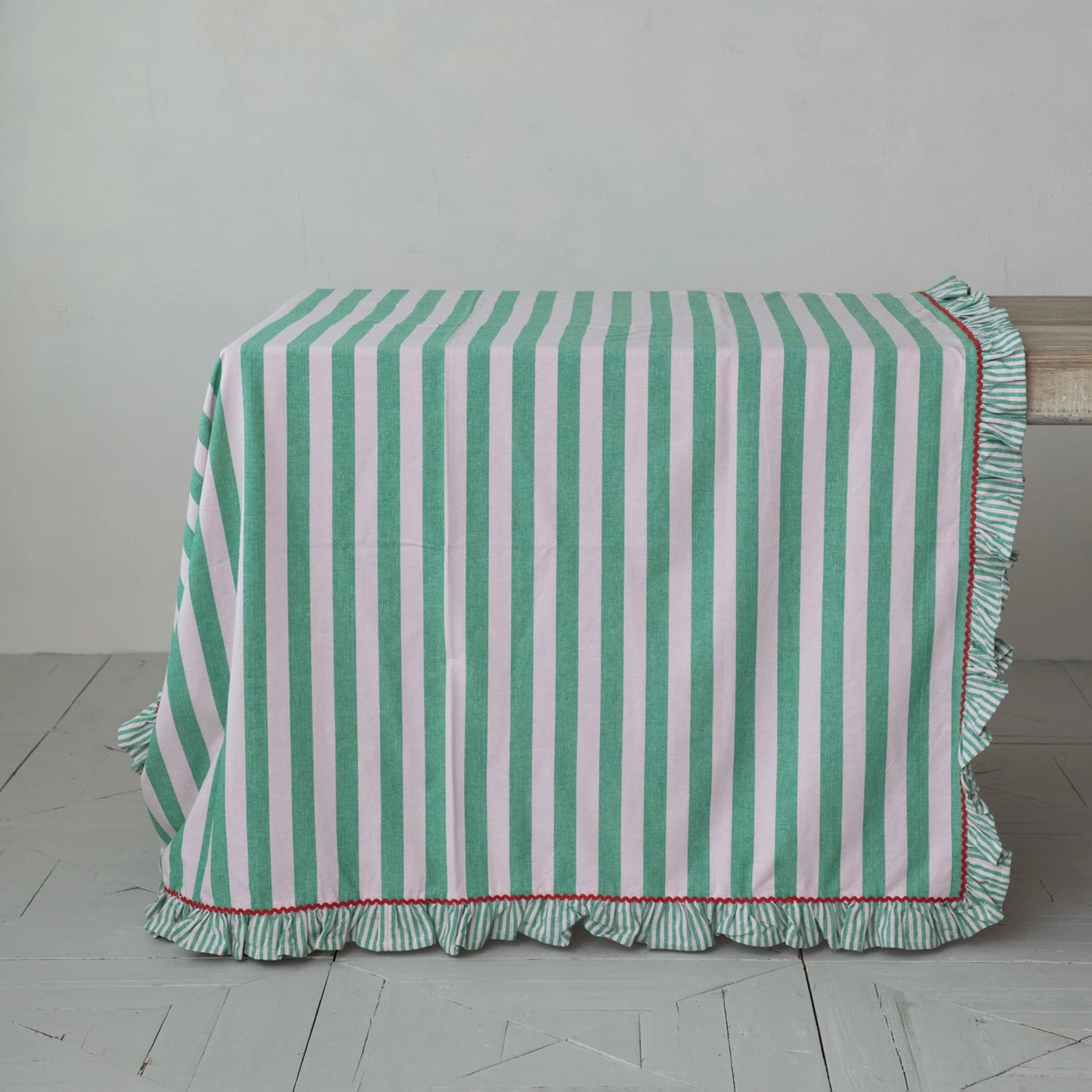 Green and pink striped tablecloth with ruffled edge and red rick rack trim on a wooden table.