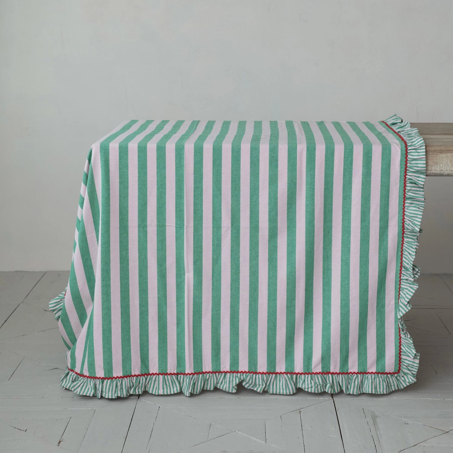 Green and pink striped tablecloth with ruffled edge and red rick rack trim on a wooden table.