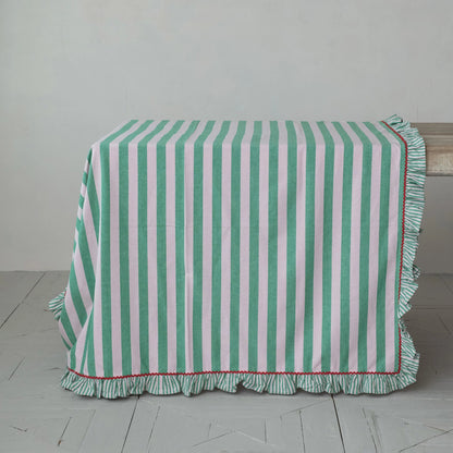 Green and pink striped tablecloth with ruffled edge and red rick rack trim on a wooden table.