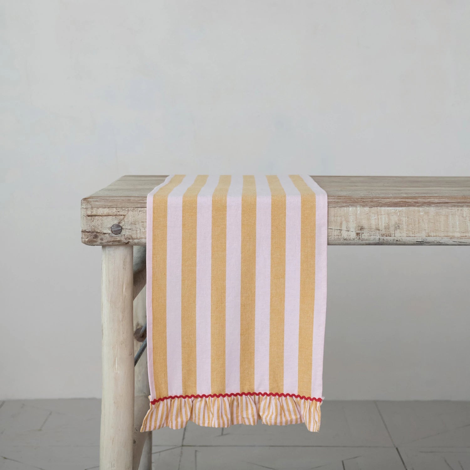 mustard and pink Striped Table Runner with Ruffle draped over the edge of a rustic wooden table