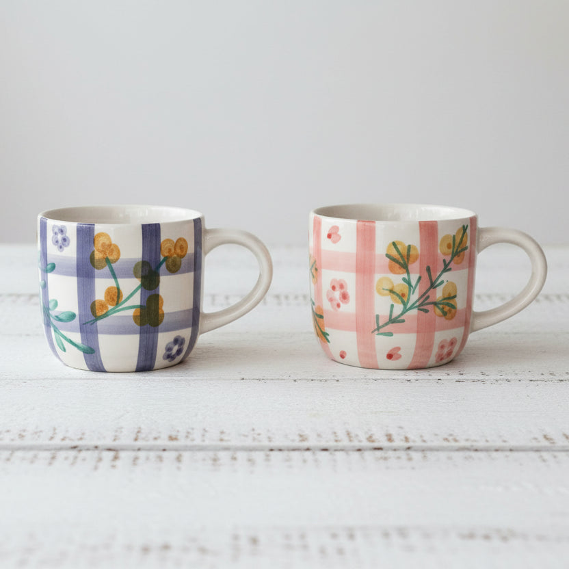 Two ceramic mugs with floral patterns on a white wooden surface