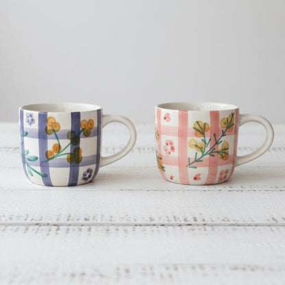 Two ceramic mugs with floral patterns on a white wooden surface