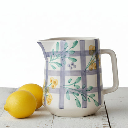 Ceramic pitcher with floral design next to two lemons on a wooden surface