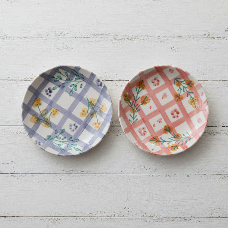 Two decorative plates with floral and plaid patterns on a white wooden background