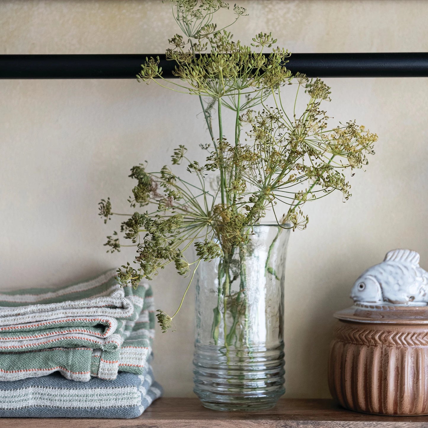 drinking glass with greenery on a shelf next to folded towels and a decorative box.