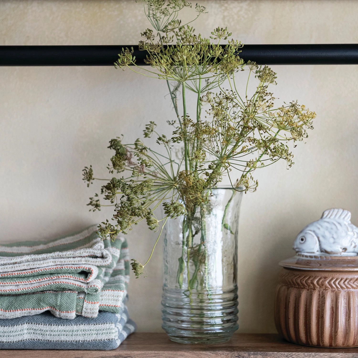drinking glass with greenery on a shelf next to folded towels and a decorative box.