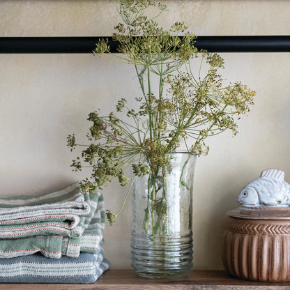drinking glass with greenery on a shelf next to folded towels and a decorative box.