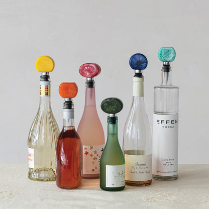 6 bottle stoppers is assorted bright colors in 6 bottles arranged on a stone surface