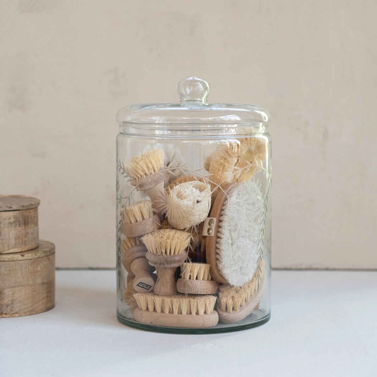 Glass jar filled with various natural brushes on a light background