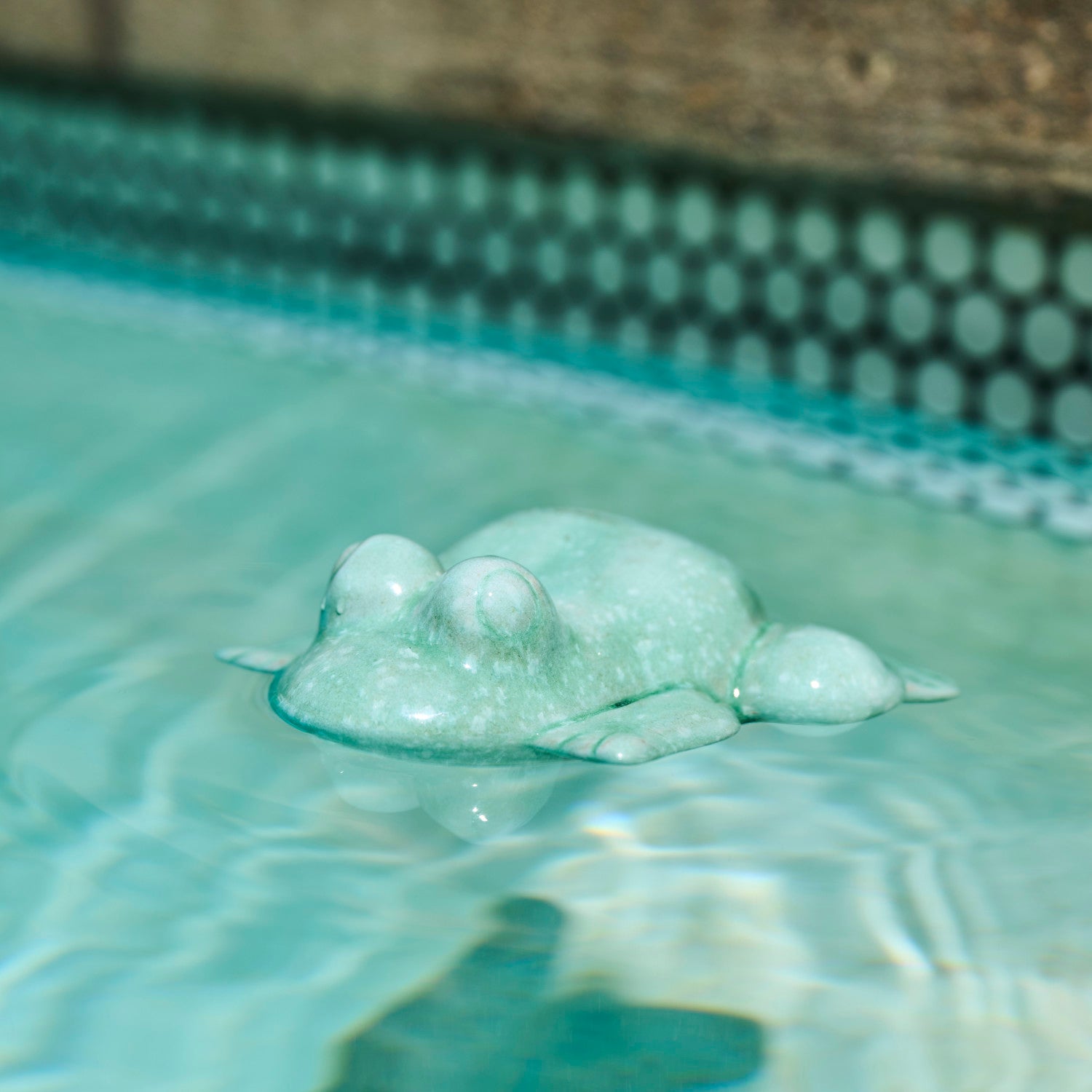 teal blue ceramic floating frog figurine in a swimming pool