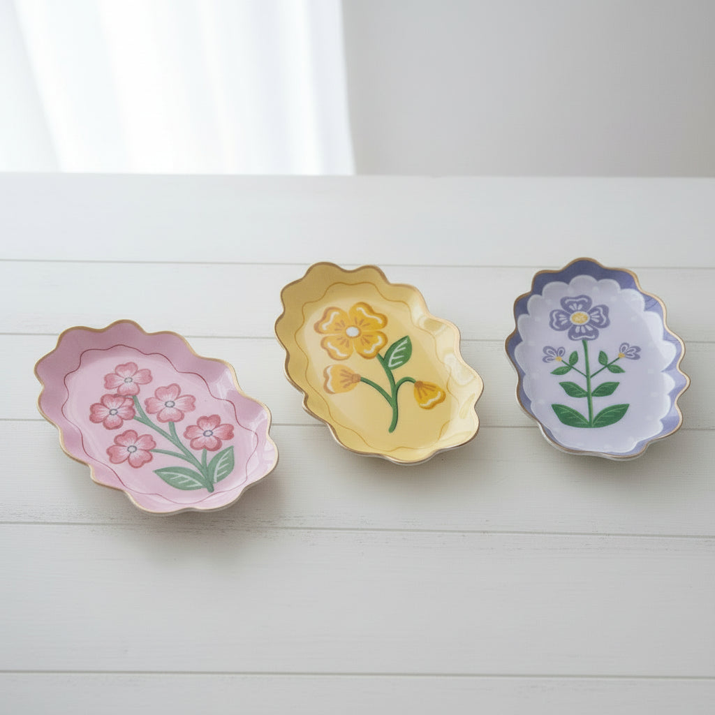 3 assorted color metal trays with flower designs on a white table