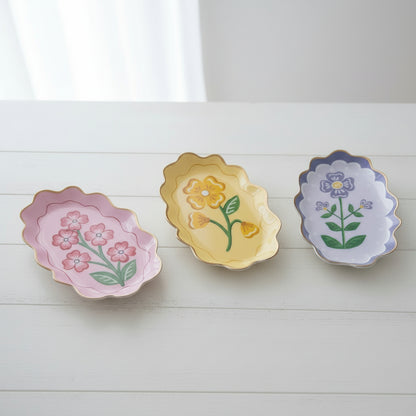 3 assorted color metal trays with flower designs on a white table
