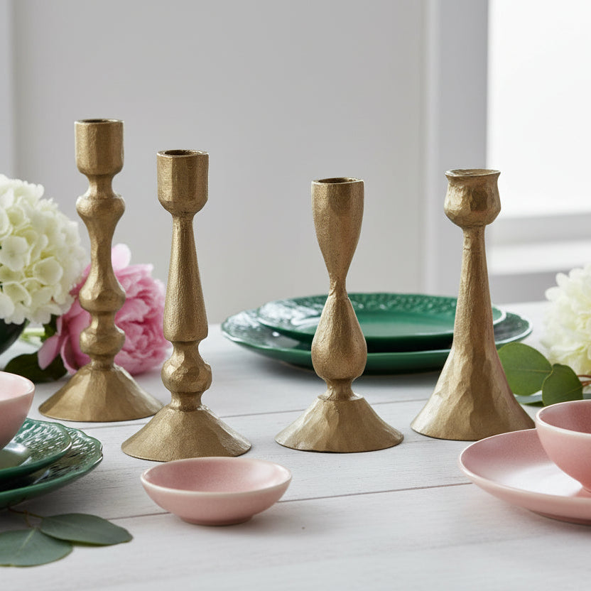 Gold candle holders on a table with pink and green dishes and flowers on a white table.