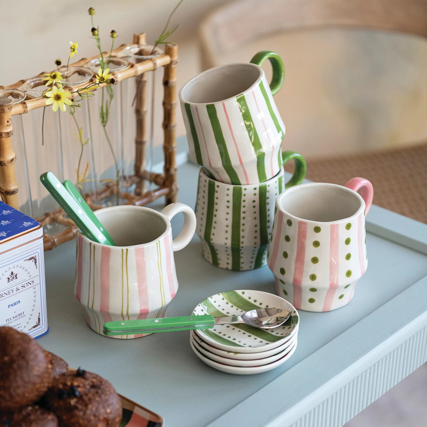 colorful mugs and plates on a tray with a box of tea and pastries.