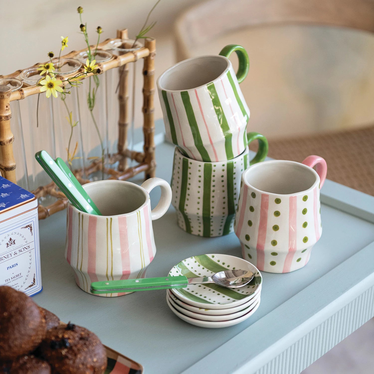 colorful mugs and plates on a tray with a box of tea and pastries.