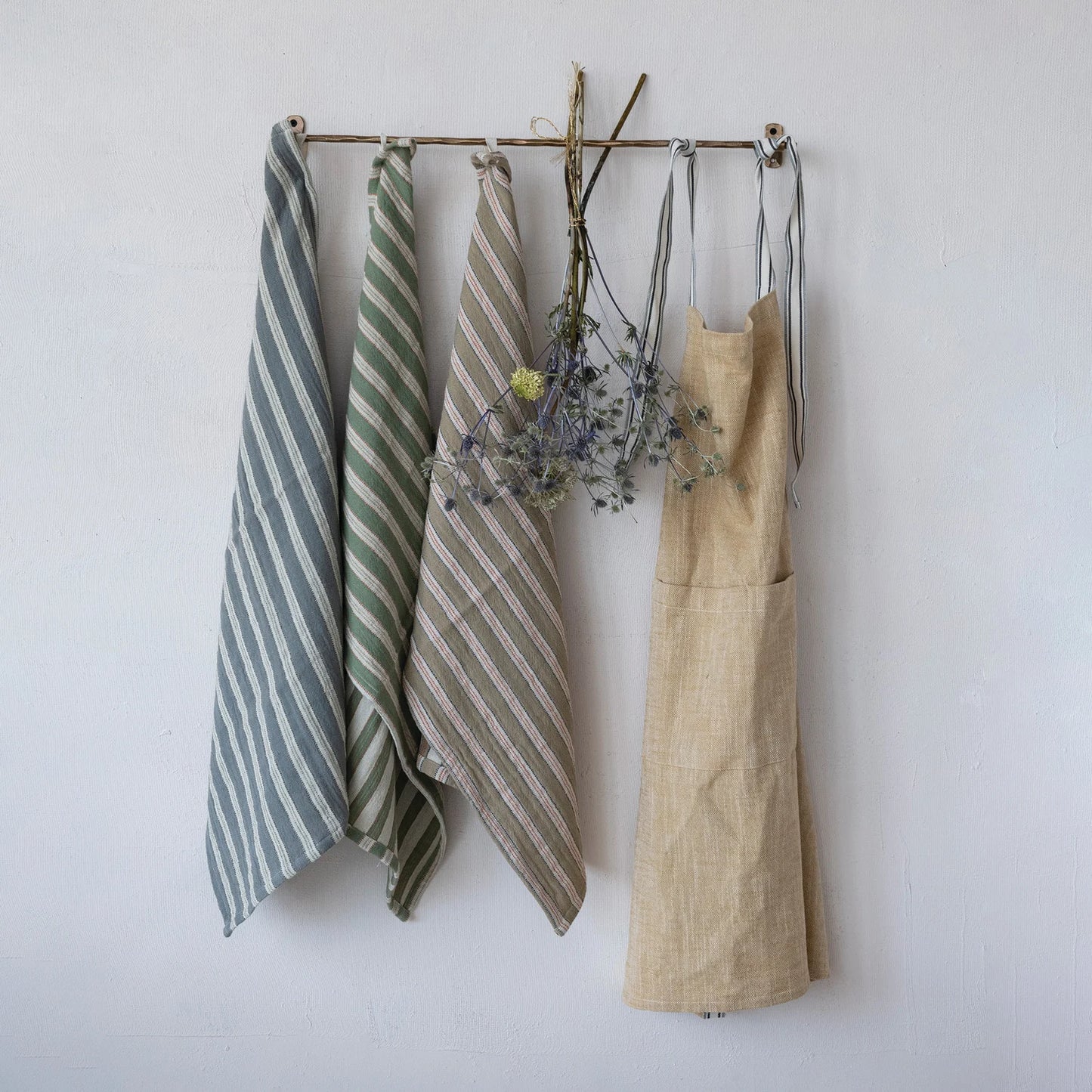 3 towels hanging from a rod next to flowers and an apron
