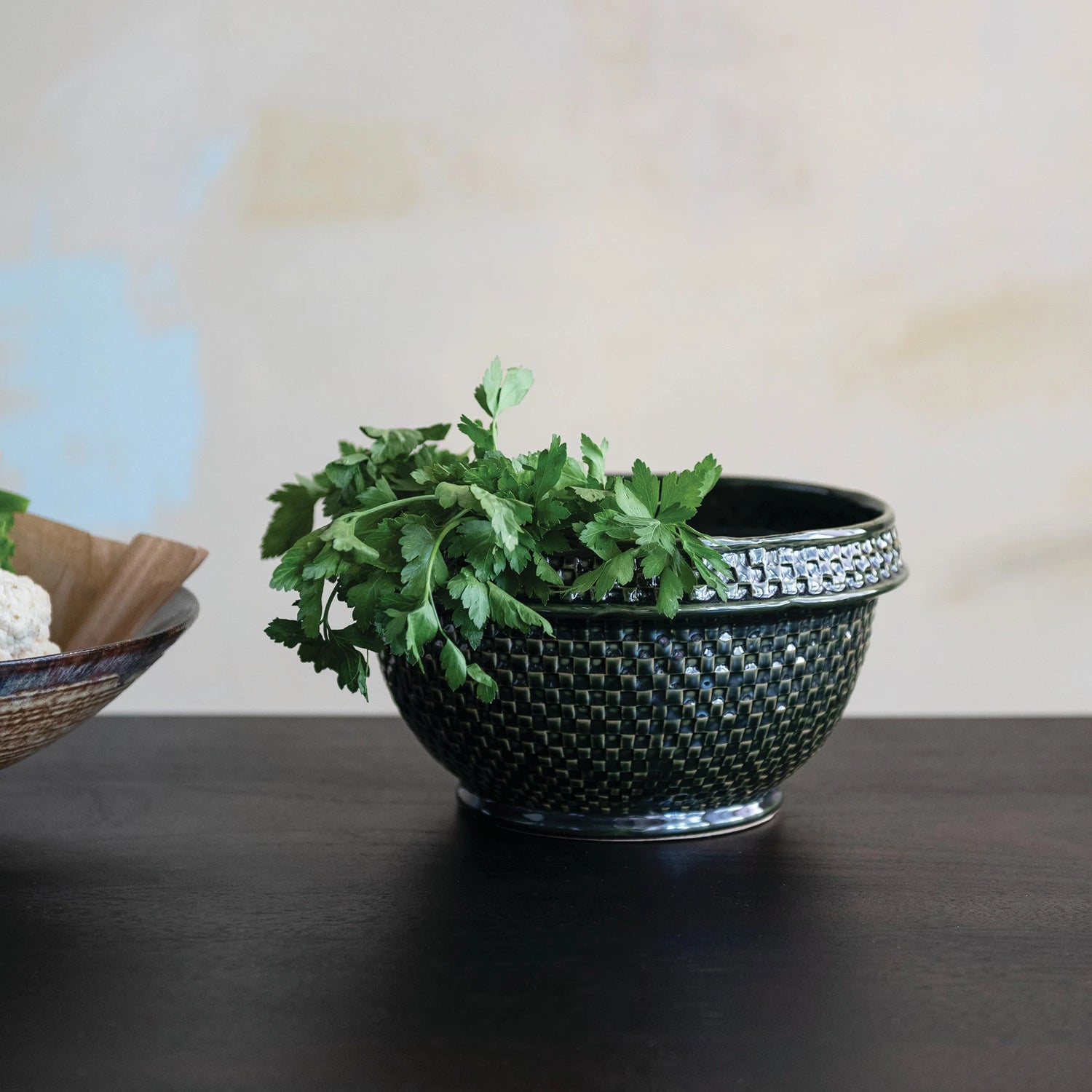 Decorative dark green woven bowl with green leaves on a dark wood surface