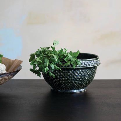 Decorative dark green woven bowl with green leaves on a dark wood surface